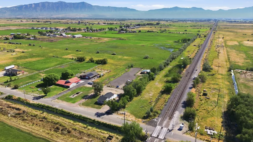 Expansive rural landscape featuring a long stretch of railroad tracks, distant mountains, and scattered residential properties