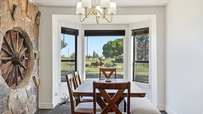Stone accent wall with wagon wheel detail, bay window with dark blinds, and a gold-finish chandelier
