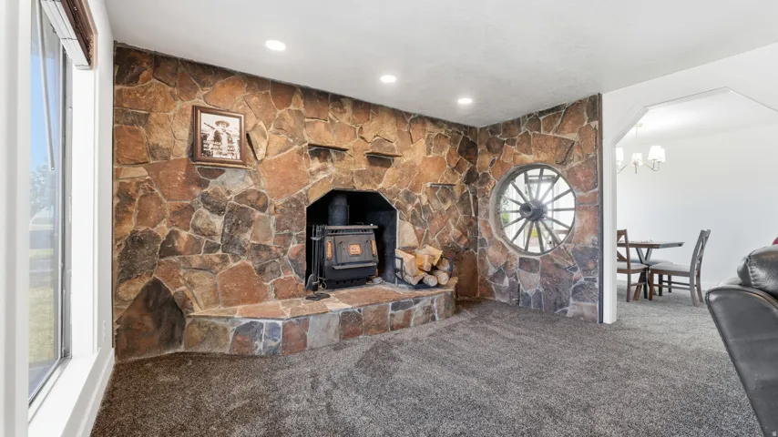 Stone-clad fireplace with a wood-burning stove and hearth, carpeted flooring, large window, and recessed lighting