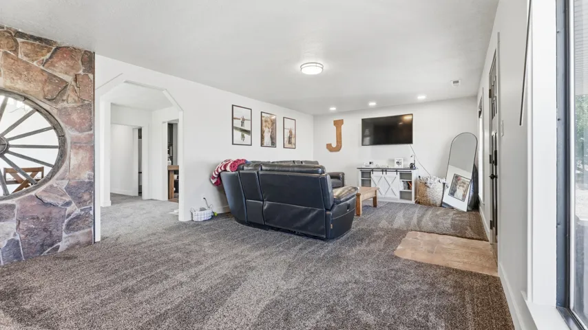 Spacious living area featuring neutral carpeting, white walls, built-in media console, recessed lighting, and a stone-clad architectural element