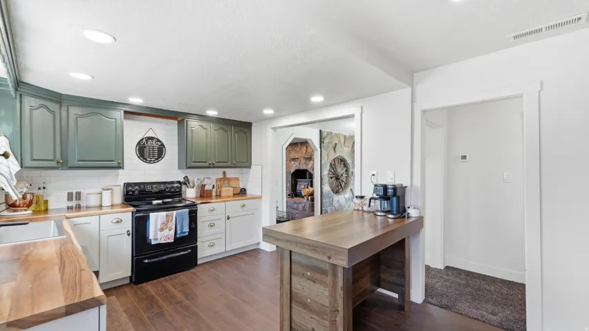 Kitchen featuring wood-finish flooring, two-tone cabinetry, wood countertops, white subway tile backsplash, and a black electric range