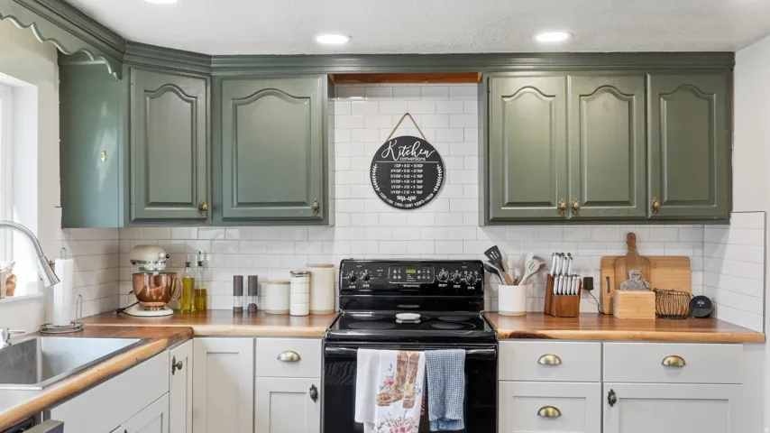 Wood countertops, white subway tile backsplash, dark green upper cabinetry, light lower cabinetry, and a stainless steel sink