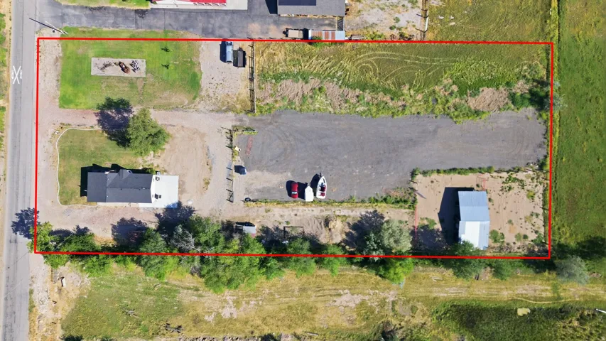 Multiple structures, including a primary residence, an additional dwelling unit, and an outbuilding, are situated on a large parcel featuring a paved driveway, a grassy area with mature trees, and undeveloped land