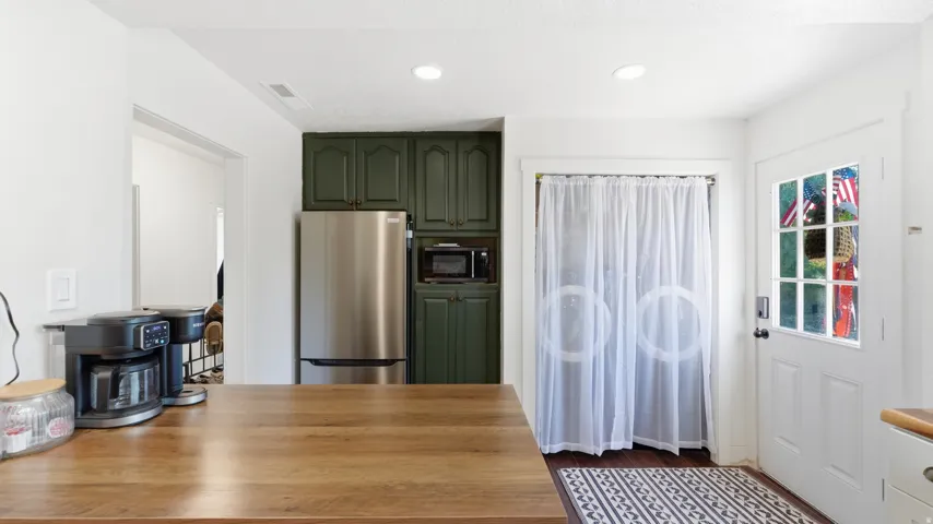 Kitchen featuring rich wood-finish countertops, dark green cabinetry, and stainless steel refrigerator