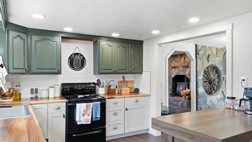 Green and light gray cabinetry, wood-finish countertops, white subway tile backsplash, recessed lighting, and a stone-clad sliding barn door