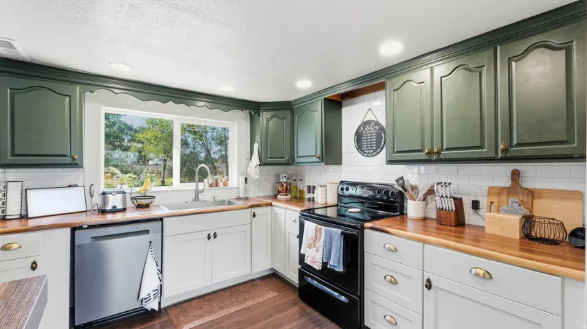 Kitchen featuring wood-finish countertops, subway tile backsplash, white base cabinetry, green upper cabinetry, and a stainless steel dishwasher