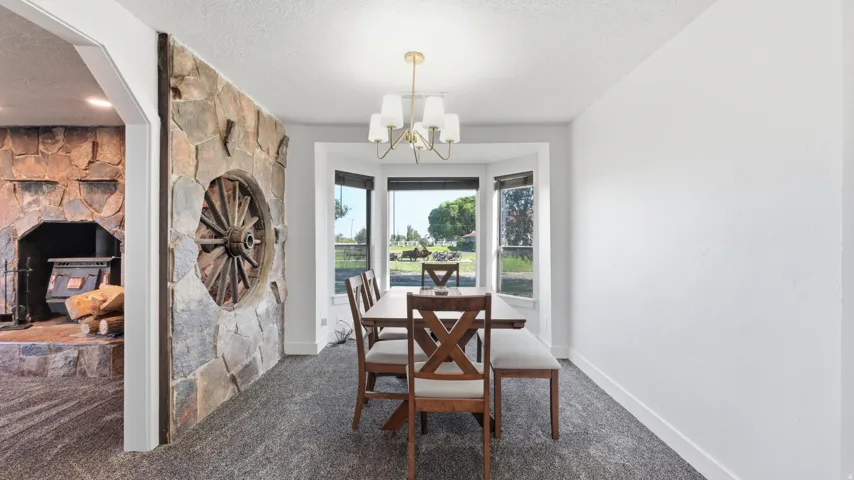 Bay window with dark trim, stone accent wall featuring a wagon wheel, and a brass-finished chandelier