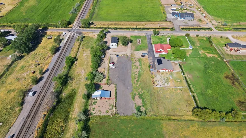 Expansive lot featuring a primary residence with a red roof, a secondary structure with a blue roof, and a large gravel area