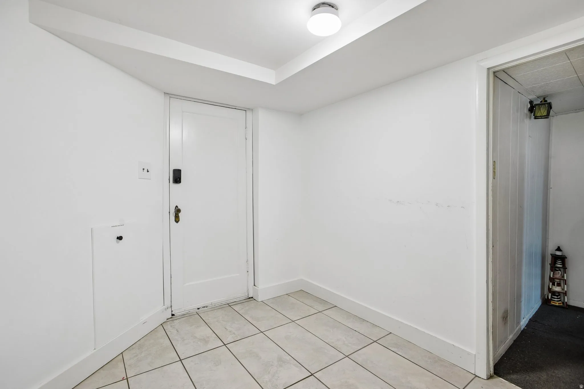 White tile flooring, flush mount ceiling light, white paneled doors, white baseboards, and white walls