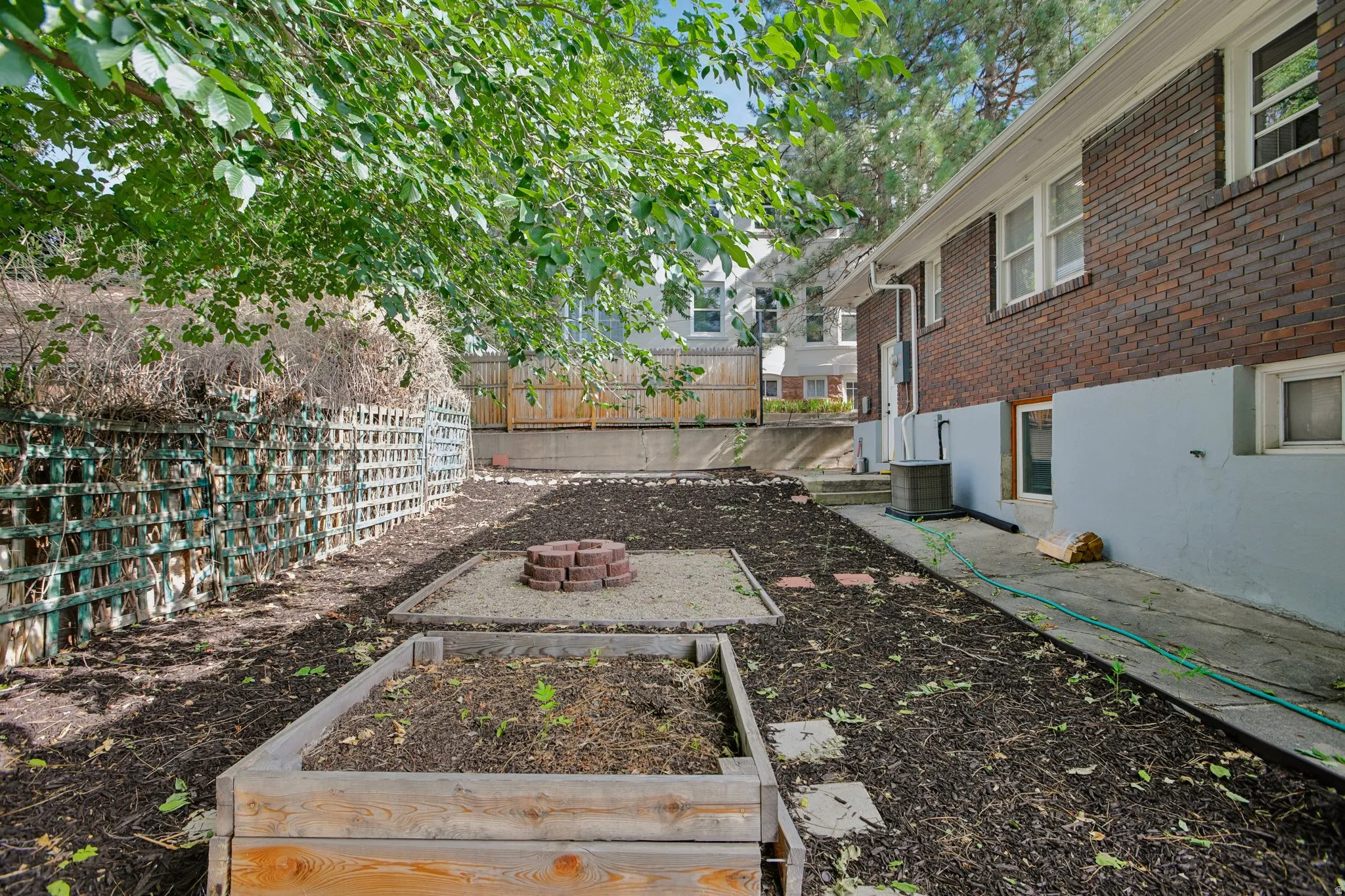 Tiered backyard with a brick exterior, two raised garden beds, a brick-ringed fire pit area, and a lattice fence