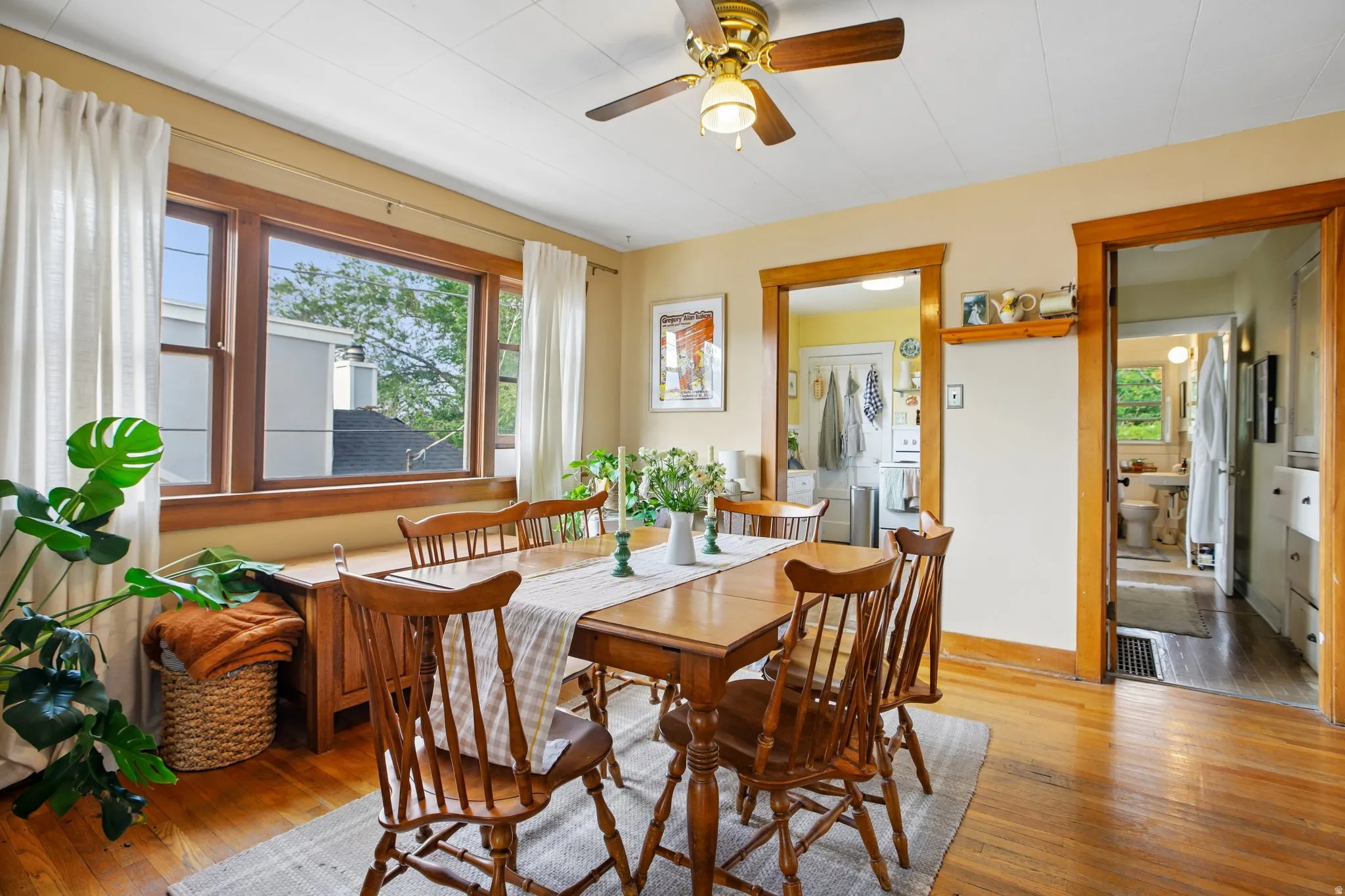 Hardwood flooring throughout, large pane window, ceiling fan, natural wood trim, and open doorways