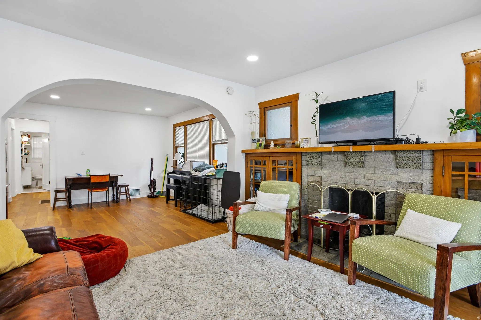 Spacious living room featuring hardwood flooring, arched architectural details, and a stone fireplace with wooden mantel