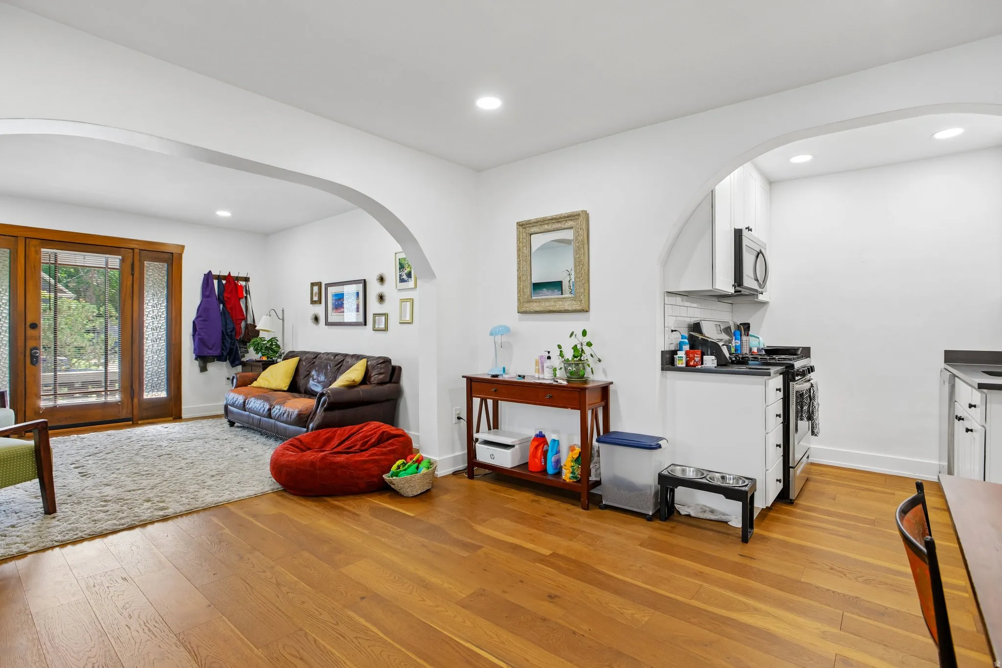Hardwood flooring, recessed lighting, arched doorways, double glass-panel doors, and a kitchen with white cabinetry