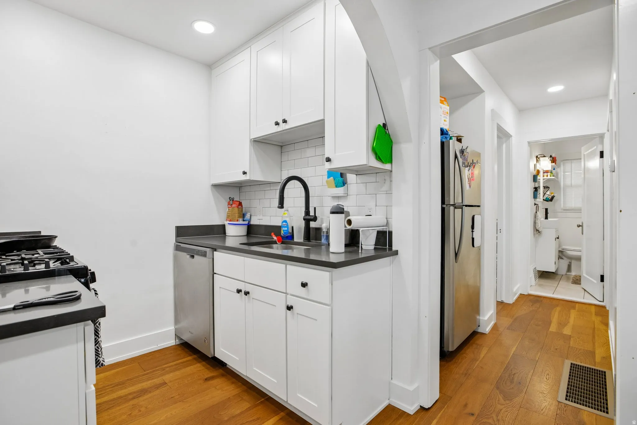 Kitchen featuring stainless steel appliances, white shaker cabinetry, dark countertops, and wood-finish flooring