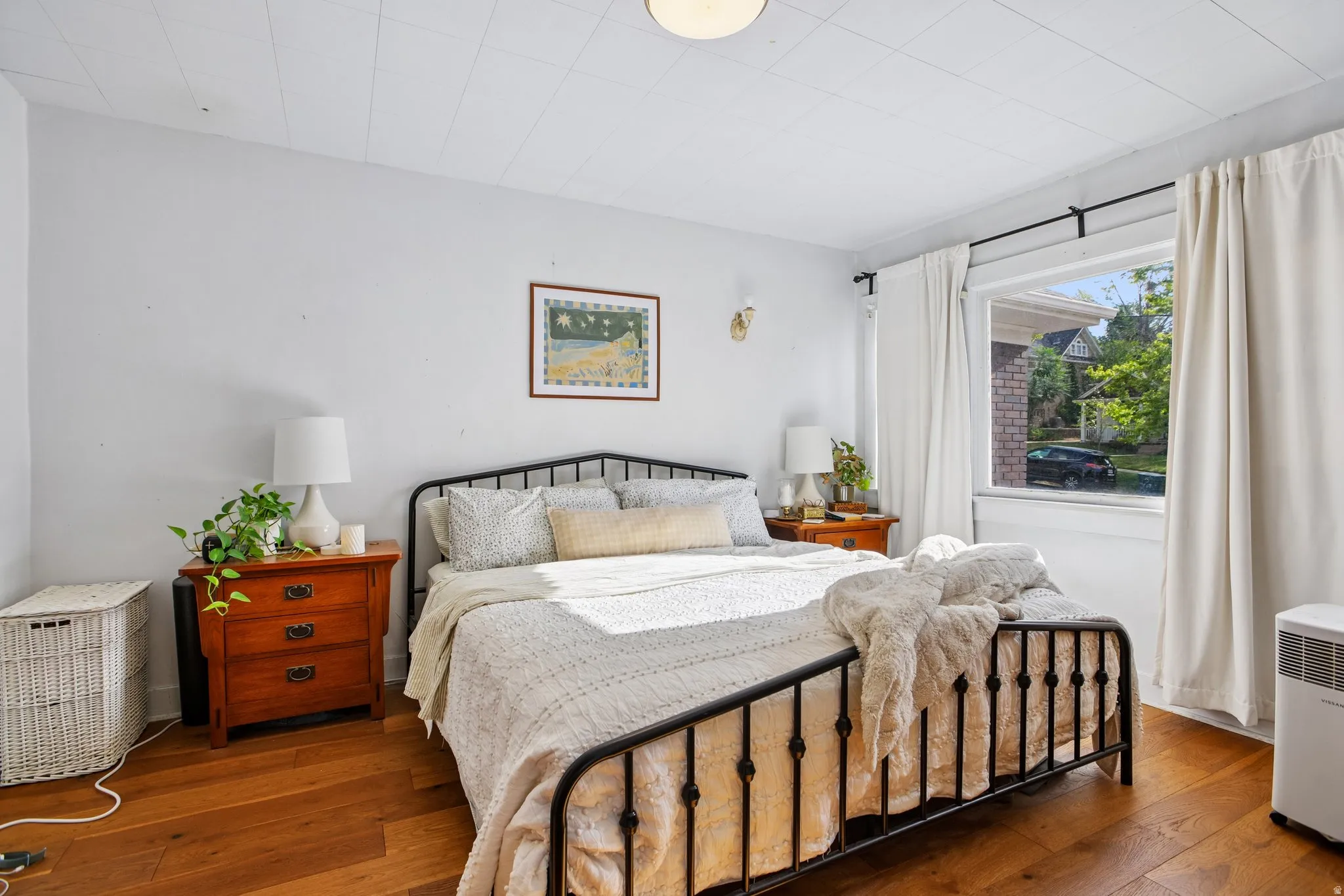 Hardwood flooring, painted white walls, ceiling with textured panels, and a large window with white trim
