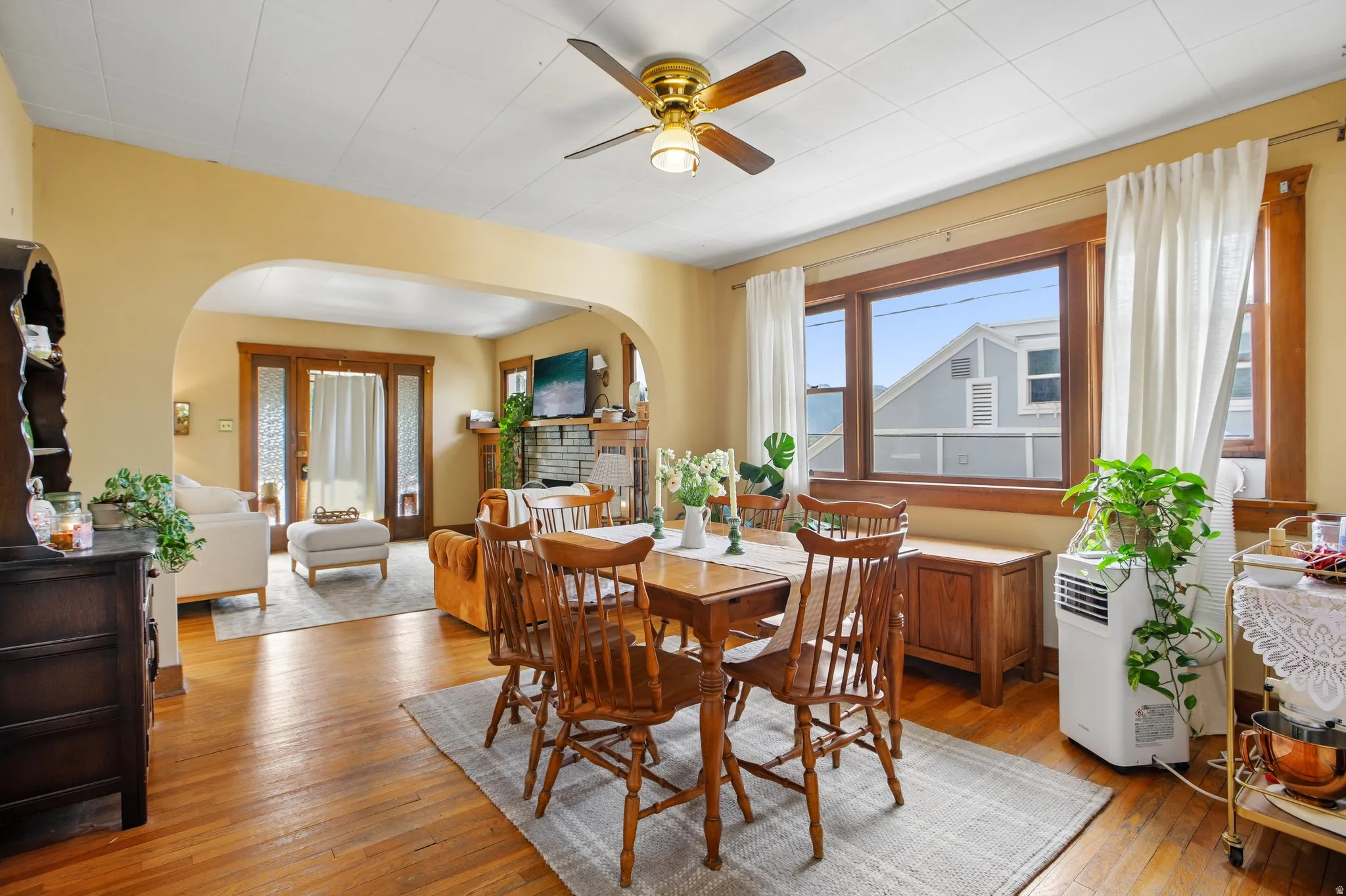 Wood-finish flooring, arched entryway, ceiling fan, and large windows with natural wood trim
