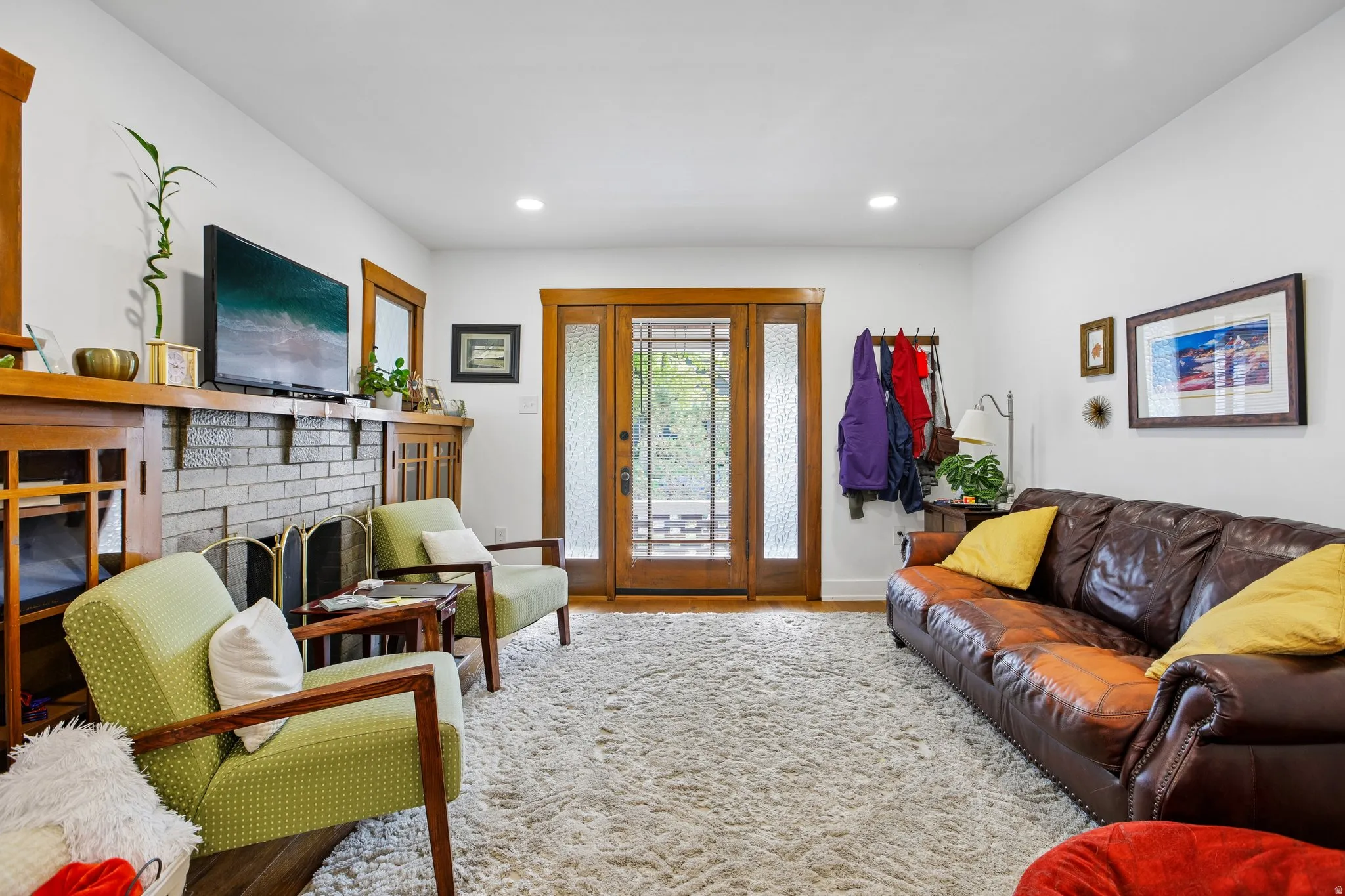 Recessed lighting, wood-trimmed entry door with privacy glass, brick fireplace with wood mantel, and wood-finish flooring