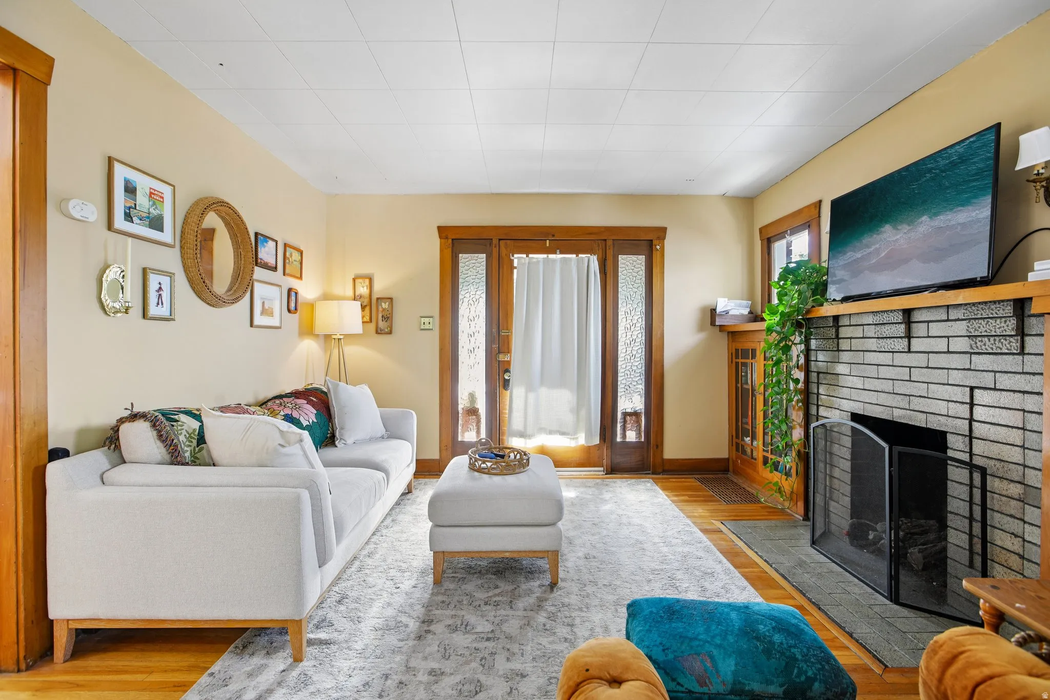 Hardwood flooring, wood trim, wood-frame glass-panel double doors, brick-surround fireplace with a wood mantle, and a built-in wood cabinet