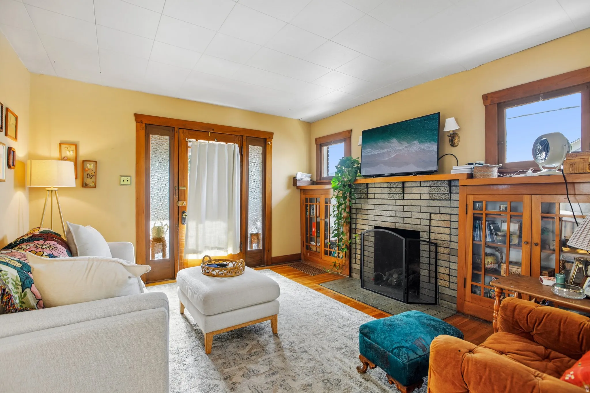 Hardwood flooring, brick fireplace with mantel, built-in cabinetry, wood-frame windows, and decorative glass panel doors