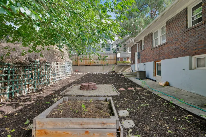 Tiered backyard with a brick exterior, two raised garden beds, a brick-ringed fire pit area, and a lattice fence