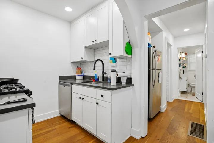 Kitchen featuring stainless steel appliances, white shaker cabinetry, dark countertops, and wood-finish flooring