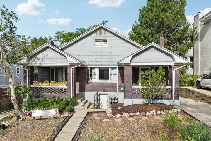 Brick and shingle exterior with dual covered entryways, a concrete walkway, and a landscaped front yard with decorative rock and mature plantings