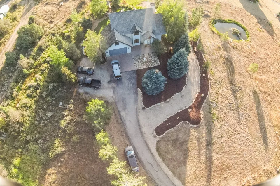 Gabled roofline with a turretted architectural feature, attached garage, paved driveway, and established landscape beds with mature trees