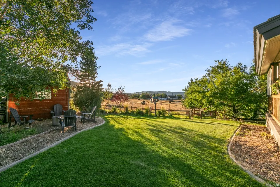 Expansive green lawn, established trees, and a gravel patio area with a detached wooden structure