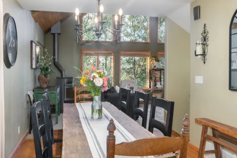 Hardwood flooring, wood-paneled vaulted ceiling, black wood stove, chandelier lighting fixture, and large windows