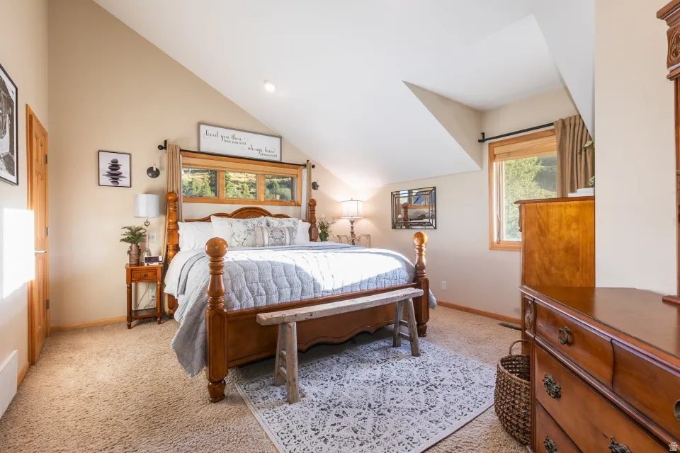 Sloped ceiling with recessed lighting, carpet flooring, and a large window with wood trim
