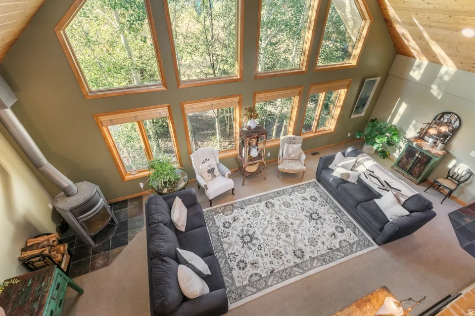 Vaulted ceilings with exposed wood beams, extensive natural wood window frames, a prominent wood-burning stove with a metal flue, and multi-toned slate-style flooring