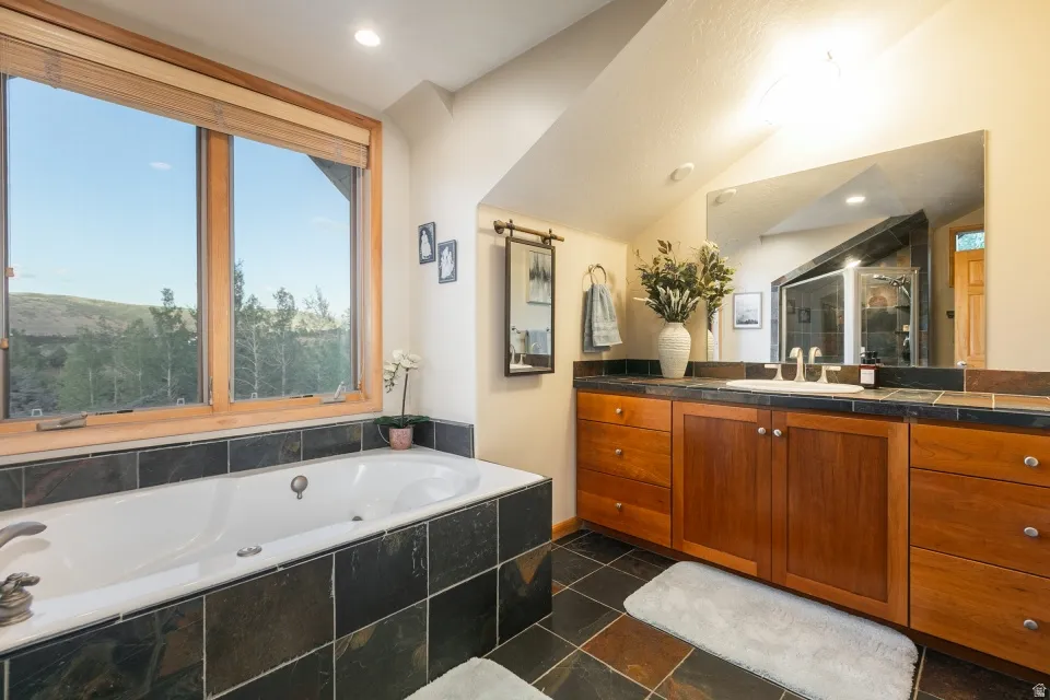 Built-in jetted tub with dark tile surround, large wood-framed window, extensive wood-finish vanity with dual sinks, and a framed mirror