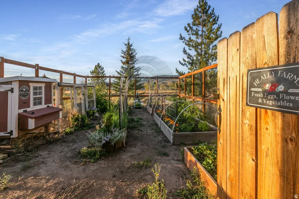 Defined garden area featuring a wooden privacy fence, multiple raised planter beds, a chicken coop, and an arched trellis