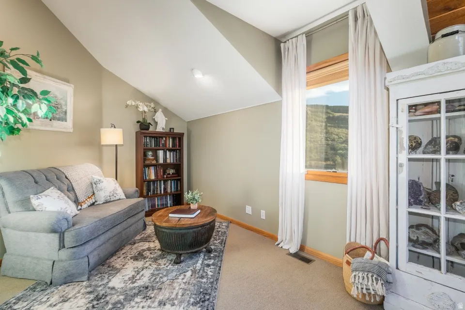 Angled ceilings, large window with natural wood trim, built-in wooden bookcase, and light neutral carpet flooring