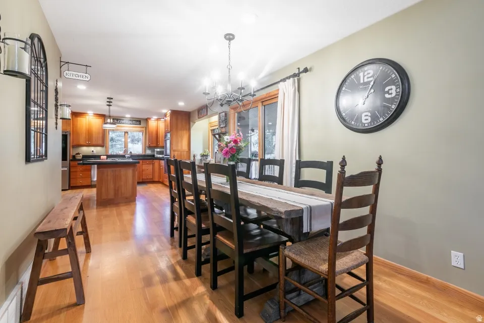 Hardwood flooring, wood cabinetry, built-in kitchen island, stainless steel appliances, and a chandelier