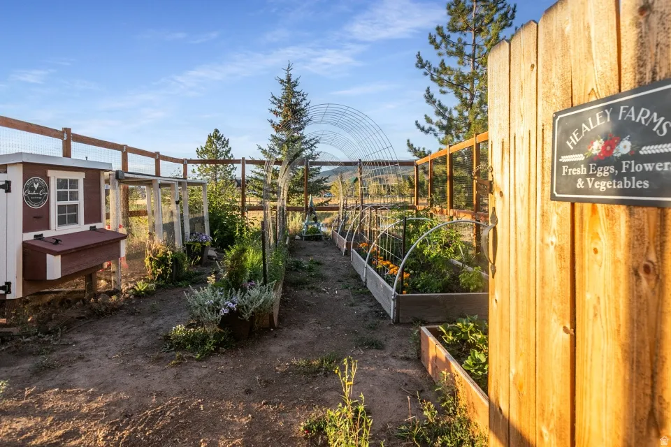 Fenced outdoor space featuring a chicken coop, raised garden beds, and an arched trellis