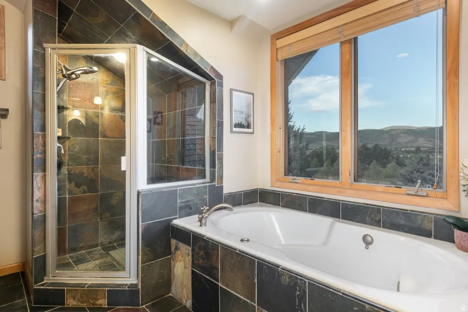 Built-in bathtub with tiled surround, adjacent to a glass-enclosed shower featuring natural stone-finish tiling