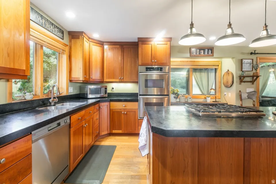 Hardwood flooring, wood cabinetry, dark countertops, stainless steel appliances, and an integrated gas cooktop