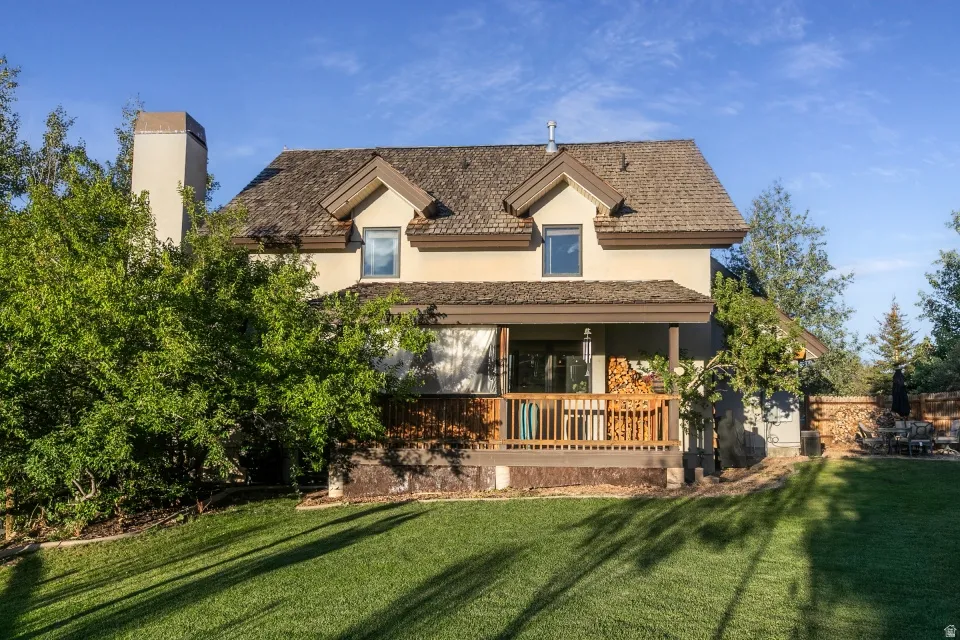 Shingle roof, stucco exterior, covered wood deck, wood railing, and manicured lawn