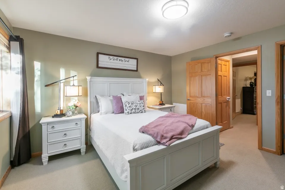 Light-colored wall-to-wall carpeting, light green wall paint, wood-framed window, wooden doors, and a flush mount ceiling light fixture