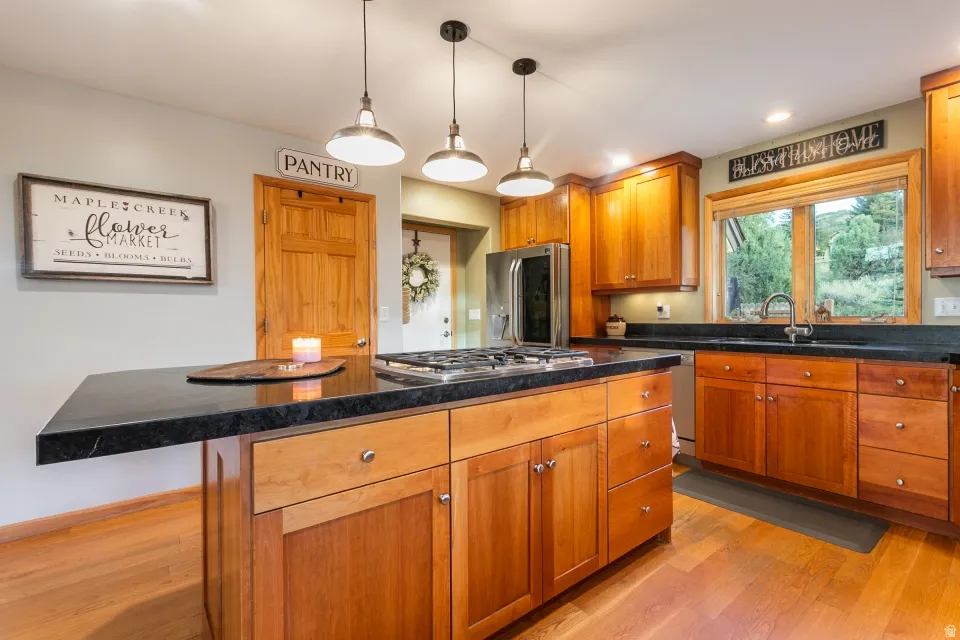 Kitchen featuring wood cabinetry, dark countertops, wood-finish flooring, stainless steel appliances, and pendant lighting
