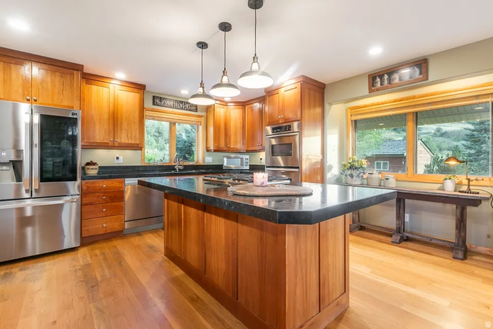 Kitchen featuring wood-finish flooring, wood cabinetry, stainless steel appliances, a center island with a dark countertop, and recessed lighting