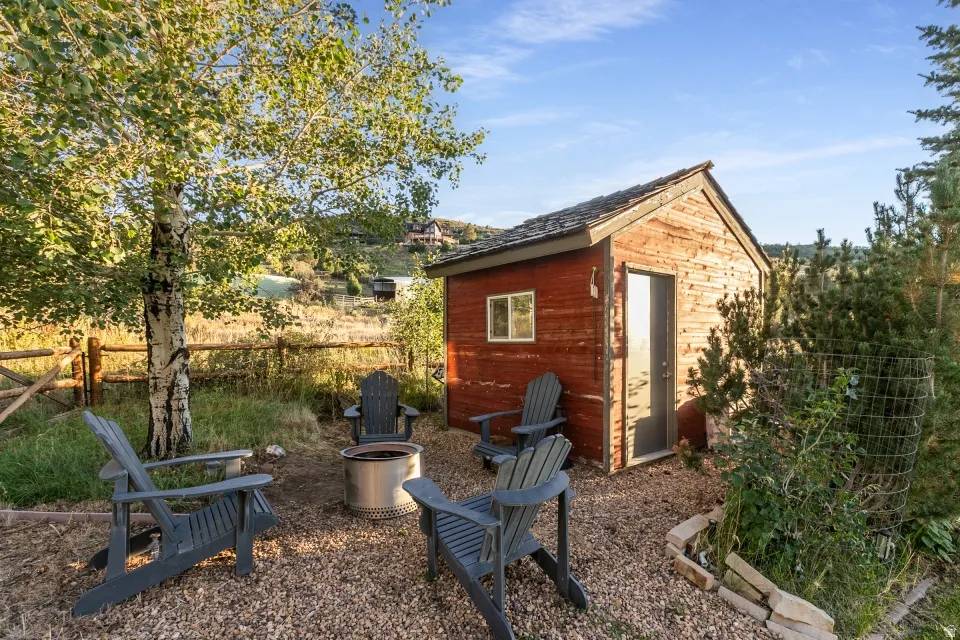 Red-sided outbuilding with shingle roof, gravel ground cover, and natural wood fencing