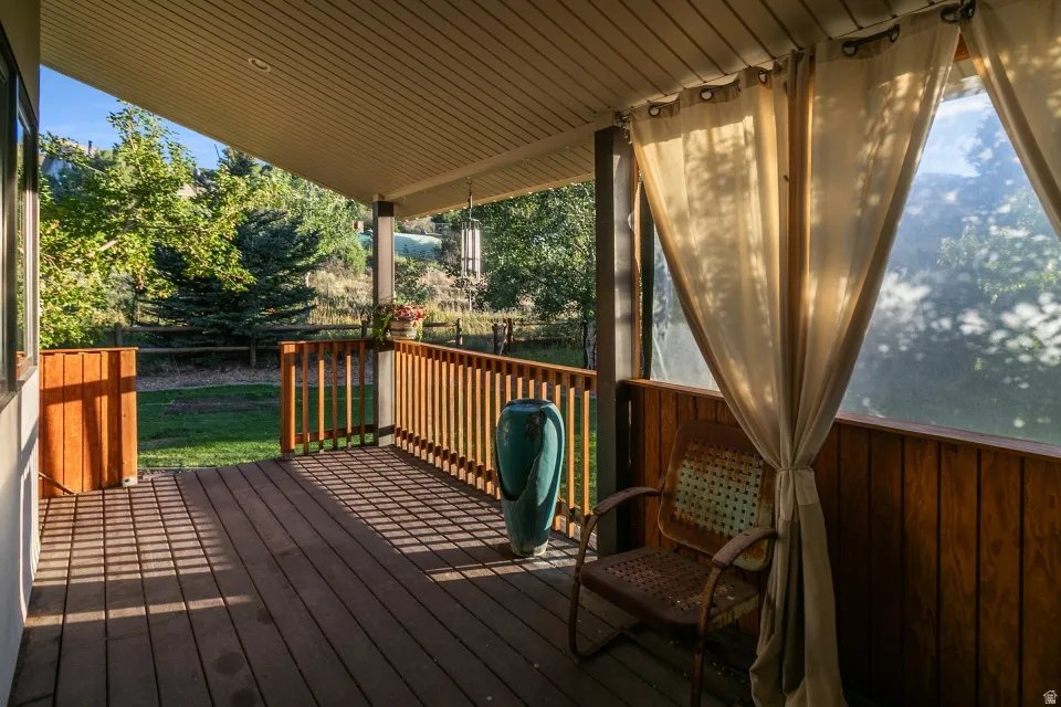 Covered porch with wood-finish decking, light wood railing, and privacy curtains