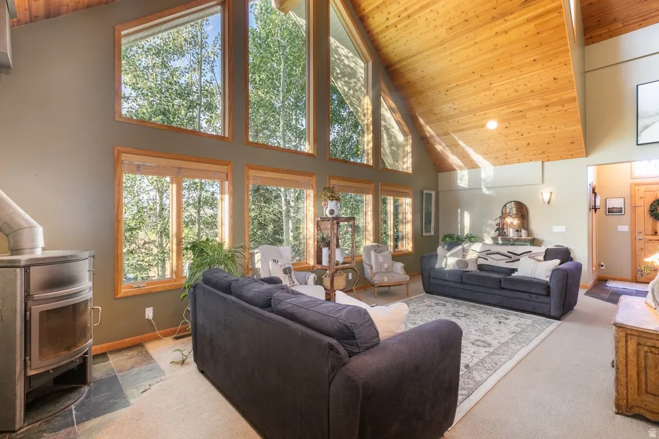 Vaulted wood-paneled ceiling, expansive windows with wood trim, built-in wood stove, and a wall of windows