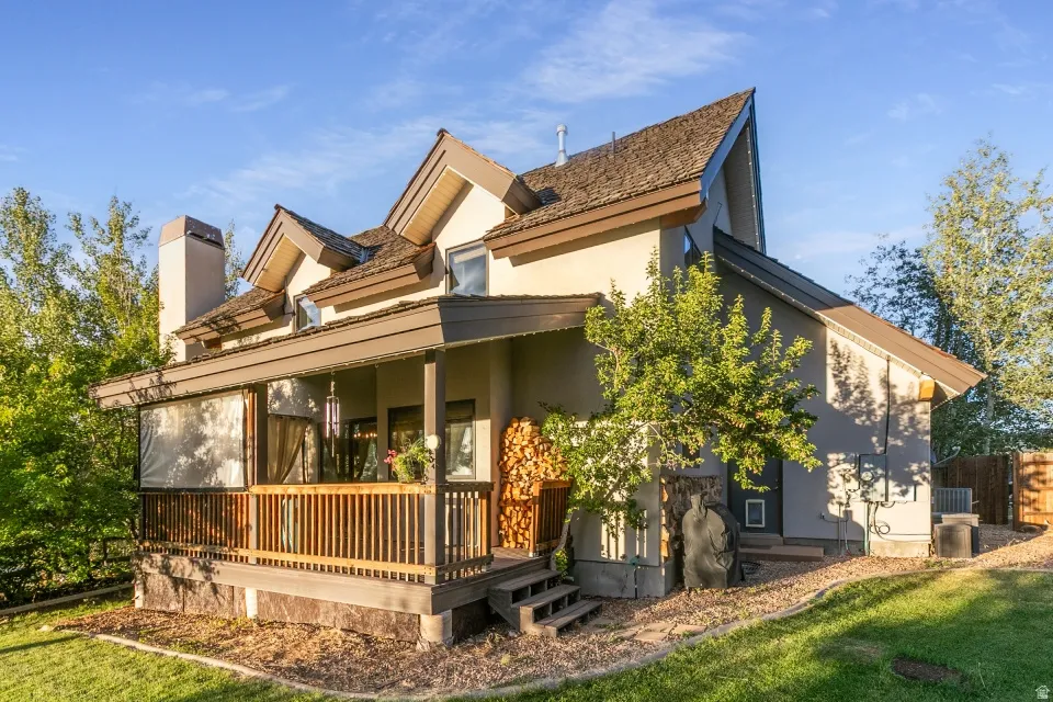 Multi-level exterior with a covered deck, wood-shingle roof, stucco siding, and an exposed chimney