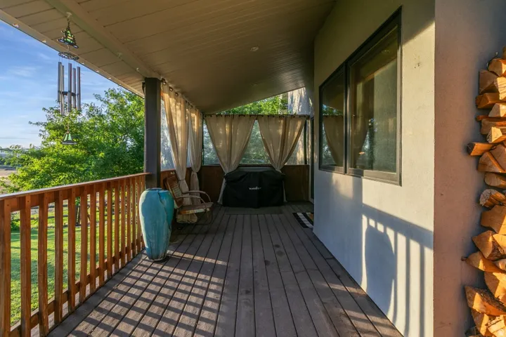 Covered deck with wood-finish flooring, wood railing, and privacy drapes
