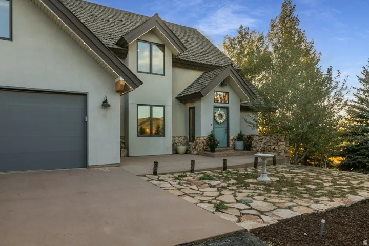 Stucco exterior with stone accents, dark gray garage door, covered entry with a light blue door, and a stone-paver pathway