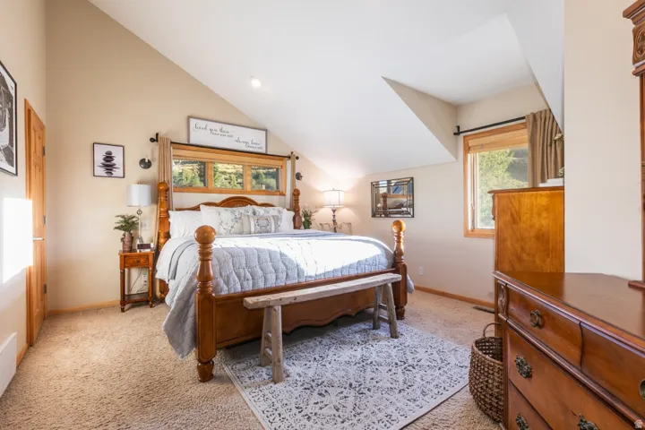Sloped ceiling with recessed lighting, carpet flooring, and a large window with wood trim