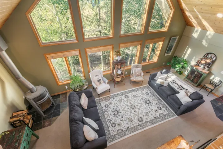 Vaulted ceilings with exposed wood beams, extensive natural wood window frames, a prominent wood-burning stove with a metal flue, and multi-toned slate-style flooring